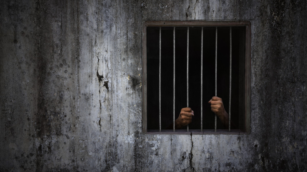 Hands of the prisoner on rusty bar of window and old grungy prison cell wall, concept of justice and horror